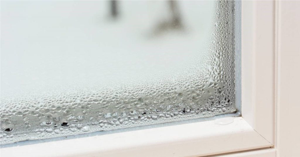 Inside of a window showing condensation on the pane and that has dripped onto the corner of the white window frame
