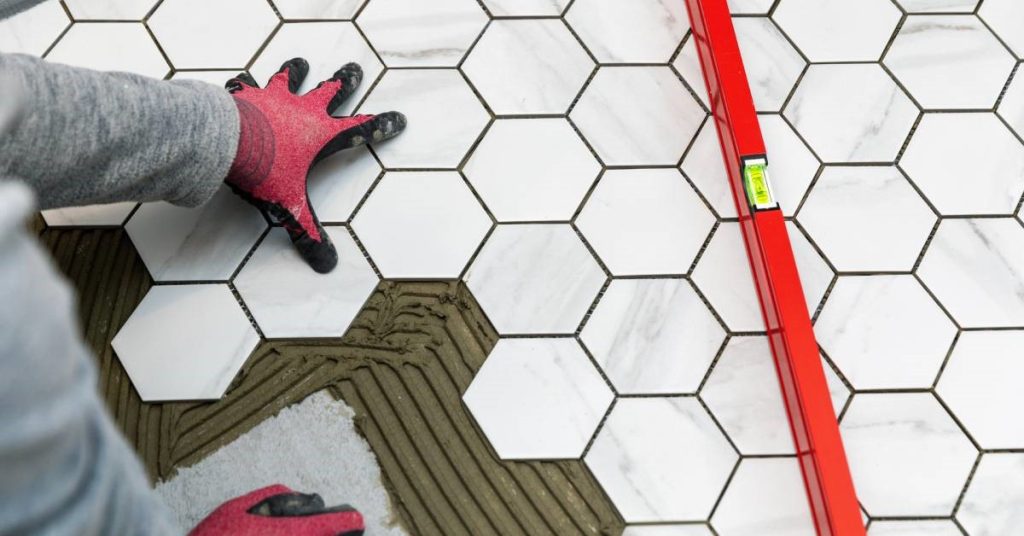 A professional home contractor expertly laying marble hexagon tiles on the floor of his bathroom remodel.