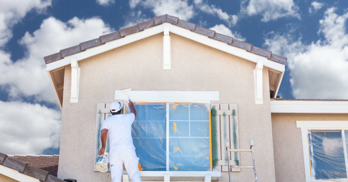 A professional contractor painting the trim and shutters of his client’s newly installed picture windows.