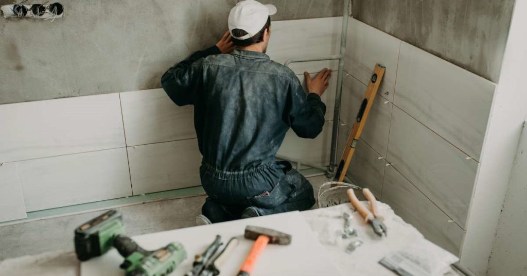 A professional contractor installing ceramic shower tiles on the bathroom wall of his client—part of larger renovations.