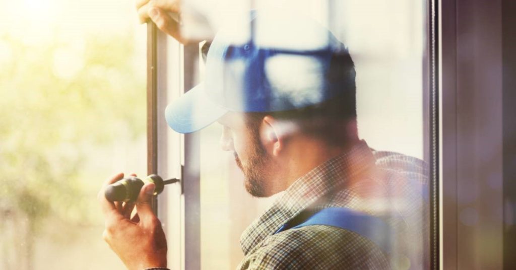 A professional contractor installing a new window. He is making adjustments to the window frame with his screwdriver.