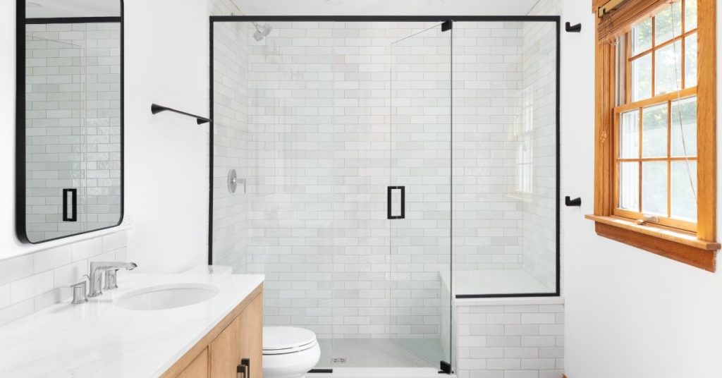 A white bathroom featuring updated hardware, including matte black metal trim around the mirror and shower door.