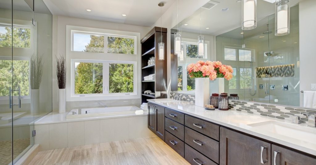 A spacious bathroom with a tub, shower, double vanity, and large mirror. The cabinetry is dark and the walls and floor are light.