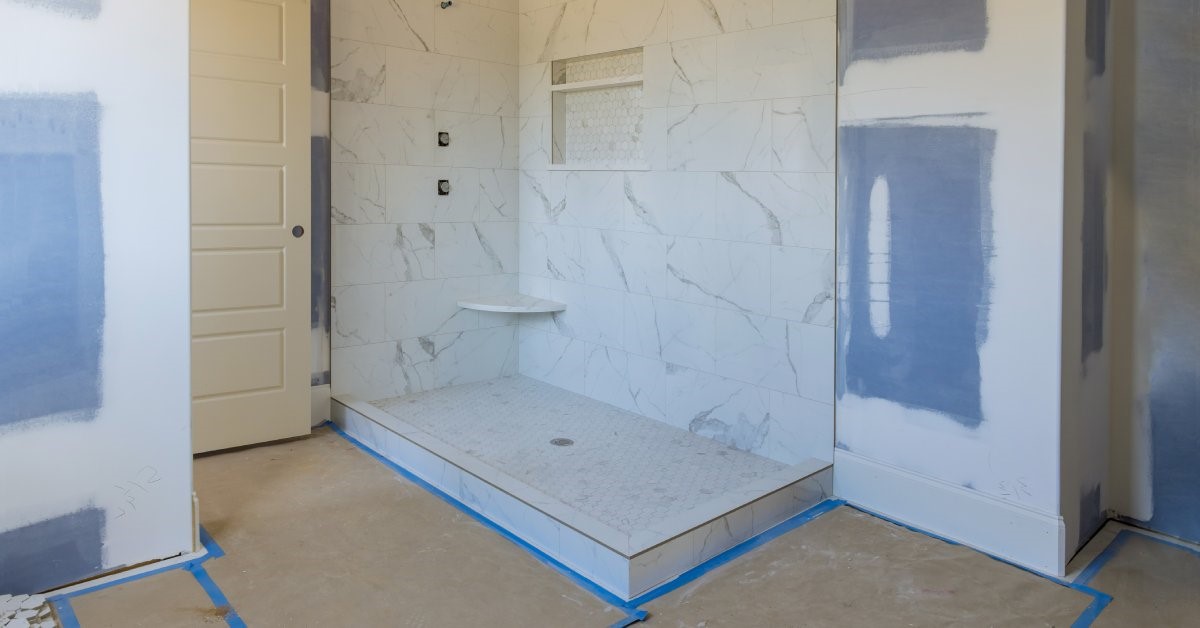 A bathroom in the process of renovations with fresh drywall. Blue painters tape marks out sections of the floor.