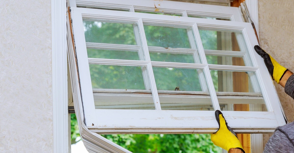The gloved hands of a professional home contractor remove an older wooden window from a client’s home.