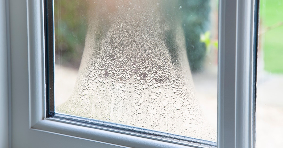 A double-glazed window. Fingerprints and condensation are on the surface of the glass. Droplets also form between the panes.