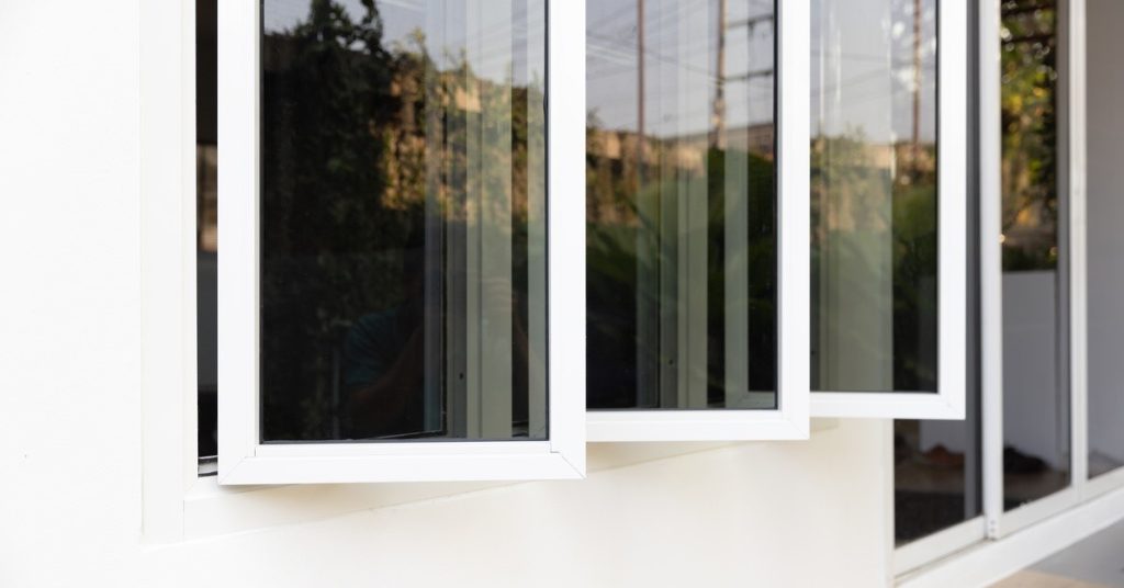 A triple-glass aluminum casement window, with all three panels open, installed against the white surface of a property.
