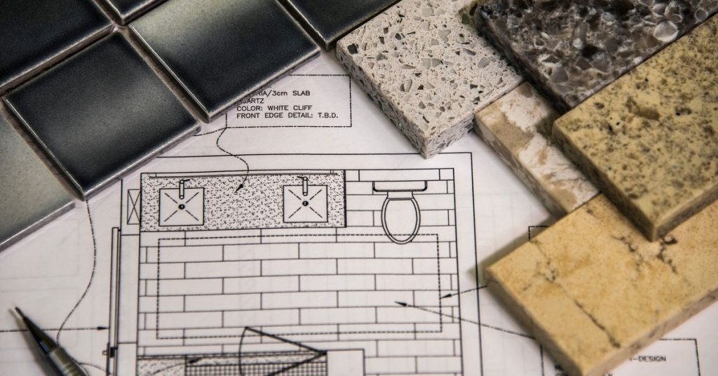 Different tiling material and design options sitting on top of a piece of paper with a sketch of a bathroom layout on it.