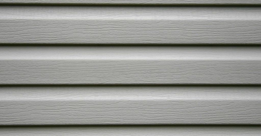 A close-up of the textured surface of neutral-colored vinyl siding on the exterior wall of a property.