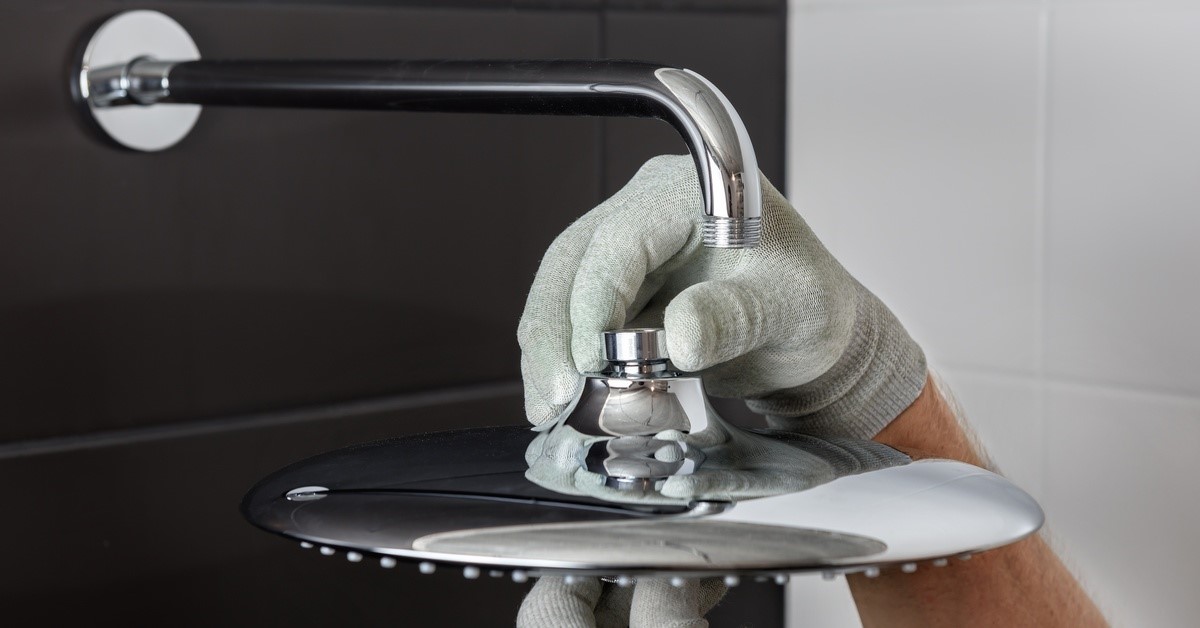 A person wearing light gray gloves using both hands to install the head of a built-in shower faucet in a bathroom.