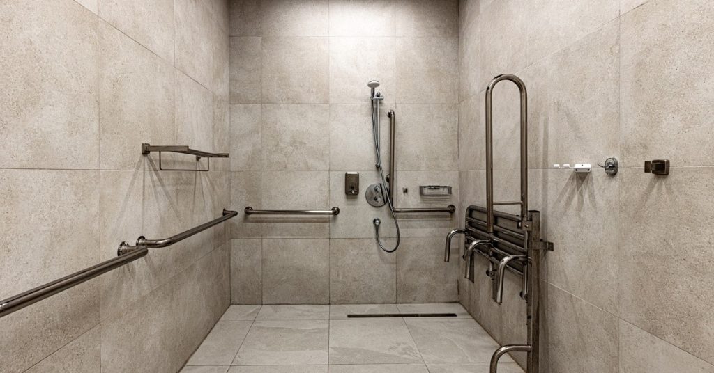 An accessible roll-in shower that has a showerhead, foldable seats, and safety grab bars installed on the walls.