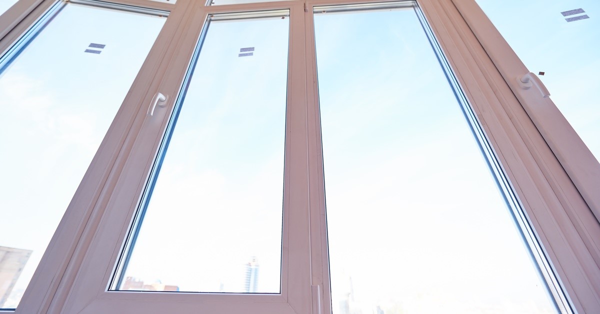 Sunlight and blue skies are visible through the glass of large casement windows that have white frames and handles.