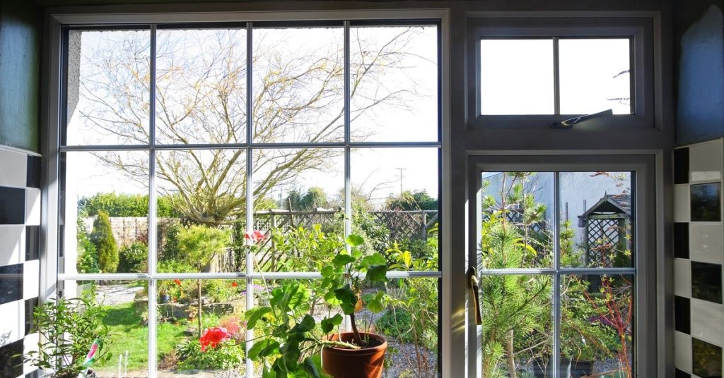 A window looking out to a garden, which is beautifully landscaped with flowers, trees, and trellises.
