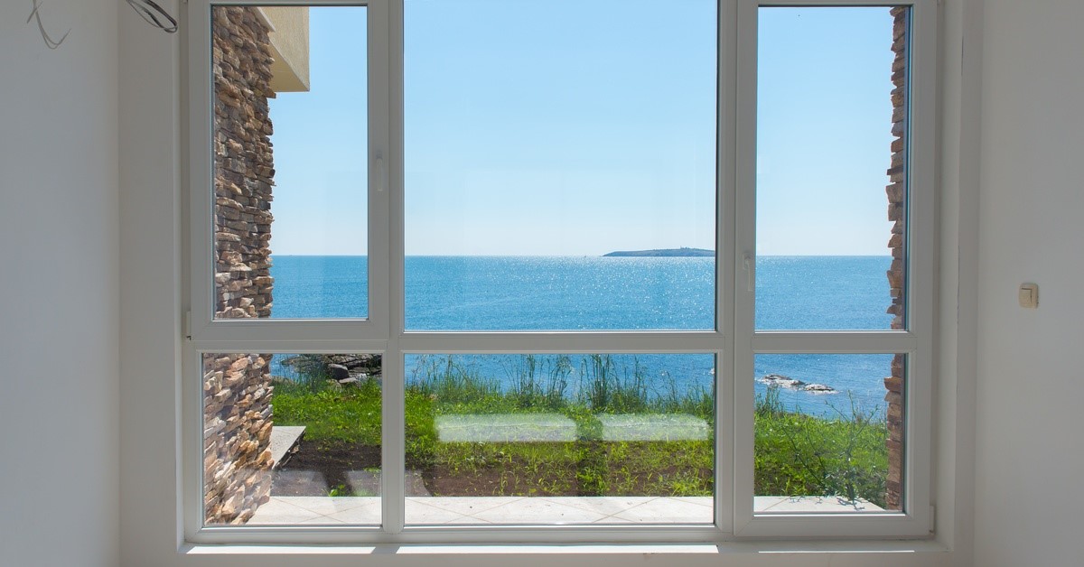A picture window look out to a body of water. There is a landmass that can be seen far in the distance in the water.