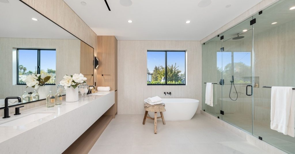 A bathroom with a bathtub against the far wall. There is a window just above the tub. There is a stool with a towel.