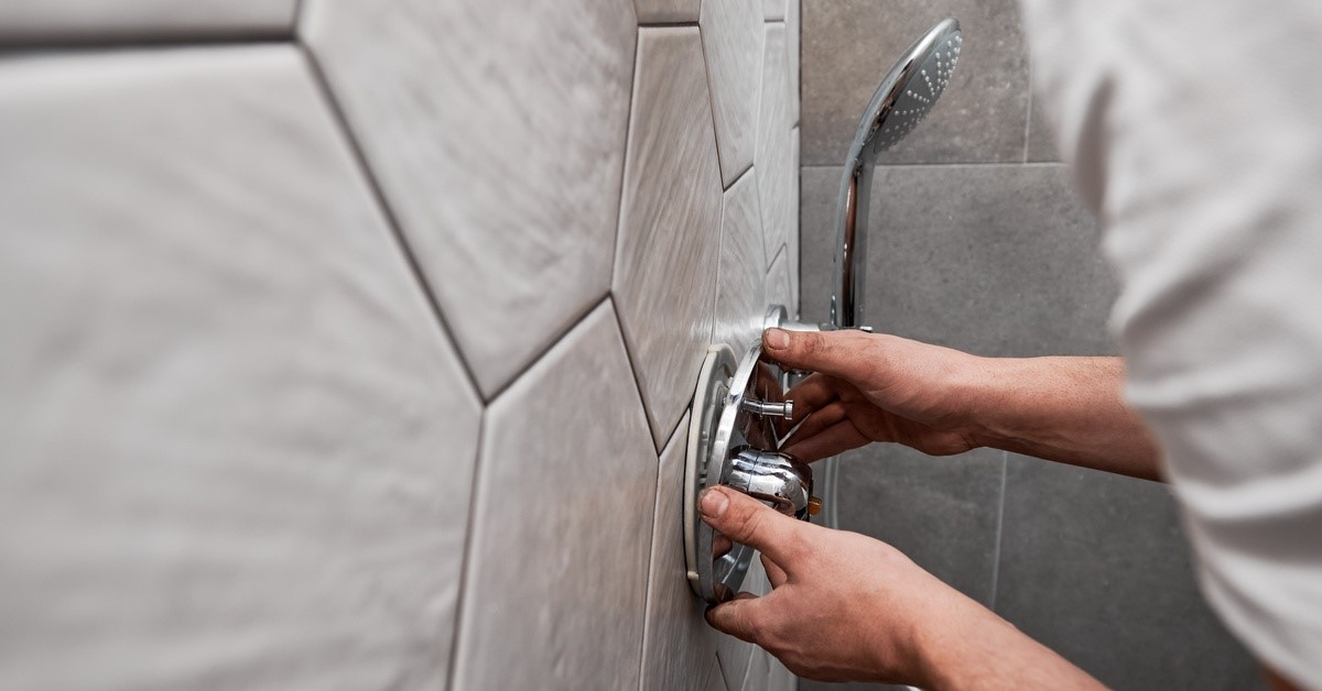Someone is installing a shower handle into a wall. The person installing it is wearing a white shirt.