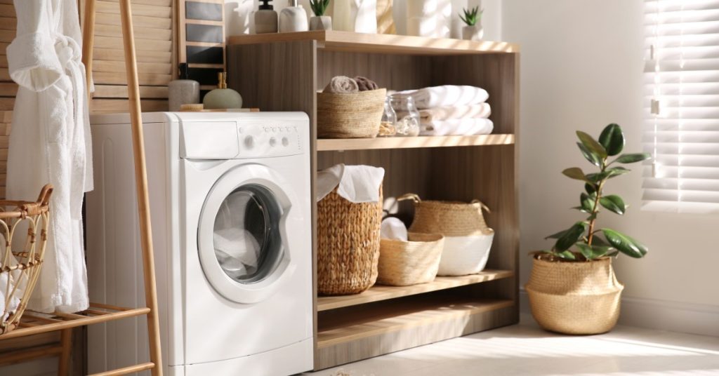 A laundry machine is next to a wooden shelf, and there is a window shining light into the room.
