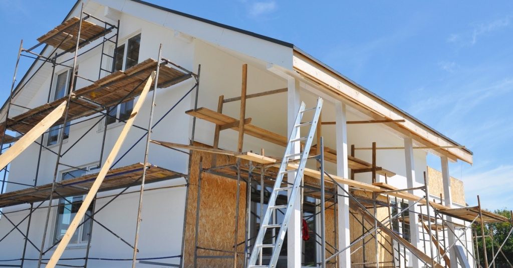 A two-story home in under construction. There is scaffolding around the home and ladder placed against it too.