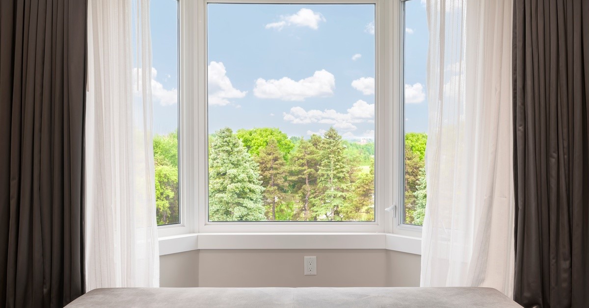 A picture window looking out to some trees. There are curtains on either side of the window.