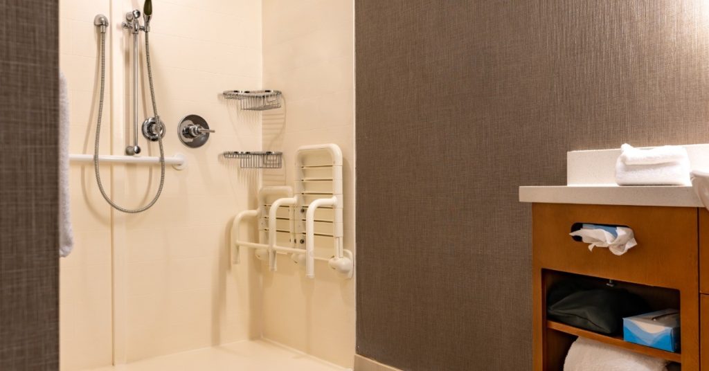A roll-in shower with warm lighting. There is a table to the right of frame with several bathroom items.
