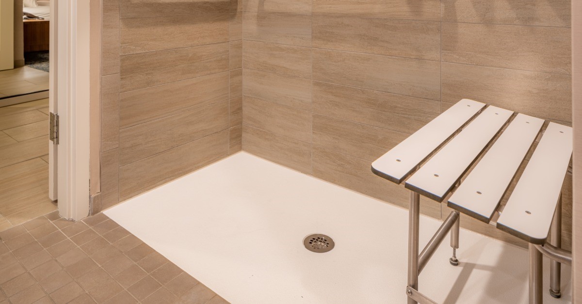 The inside of a shower with a stool to the right of frame. There are hand rails around the shower.