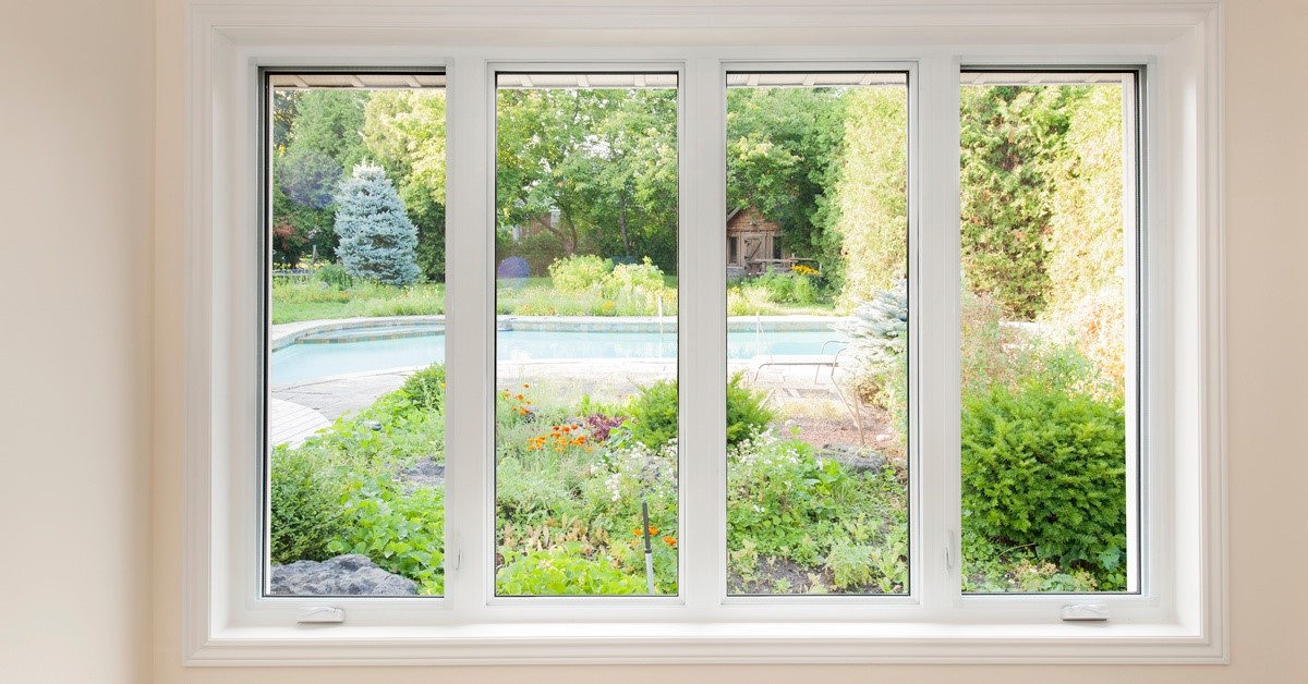 Four vertical windows are in a row. They are looking out to a backyard with trees and grass.