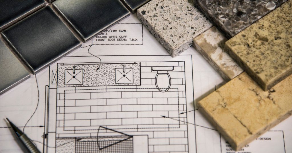 A piece of paper with a diagram of a backsplash is sitting on a flat surface, and there are several tiles on top of that paper diagram.