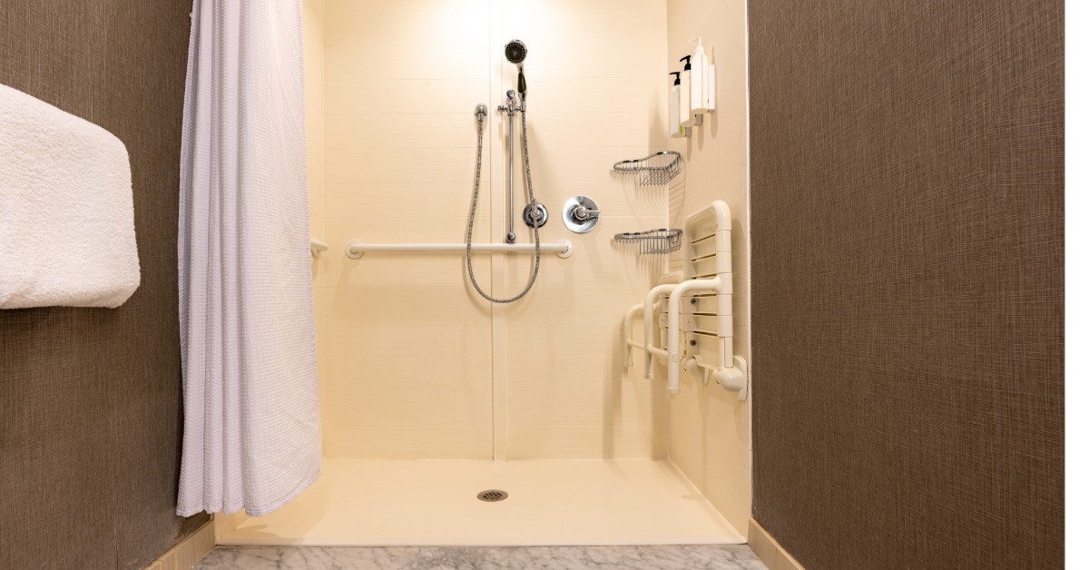 A shower with the curtain pulled back and a detachable shower head. There is a towel on a bar to the left of frame.