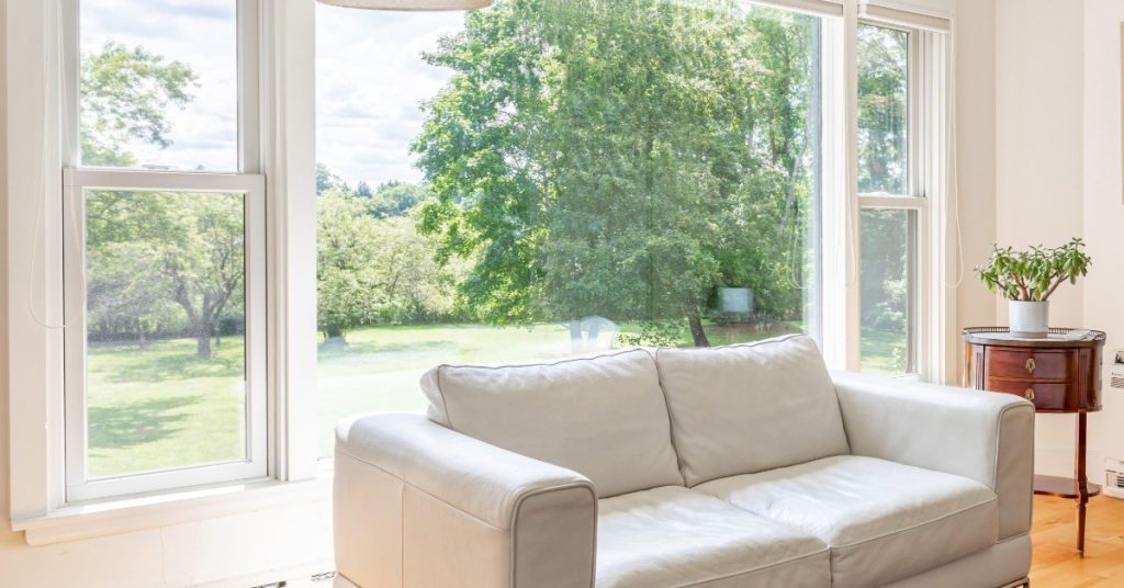 A residential living room has a large picture window behind a couch, letting in natural sunlight into the home.