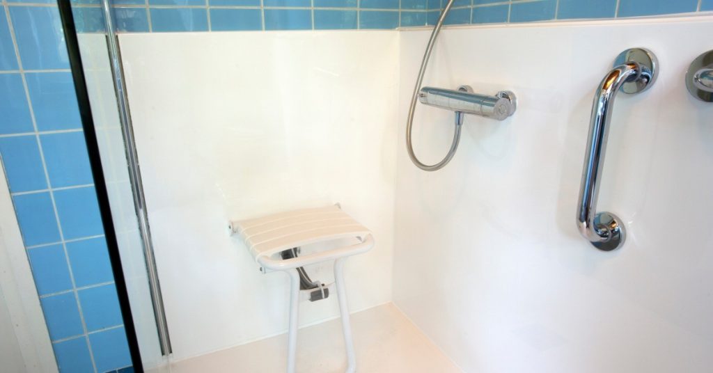 A handicap shower with a bench installed into the wall. There is a hand hold attached to the adjoining wall.