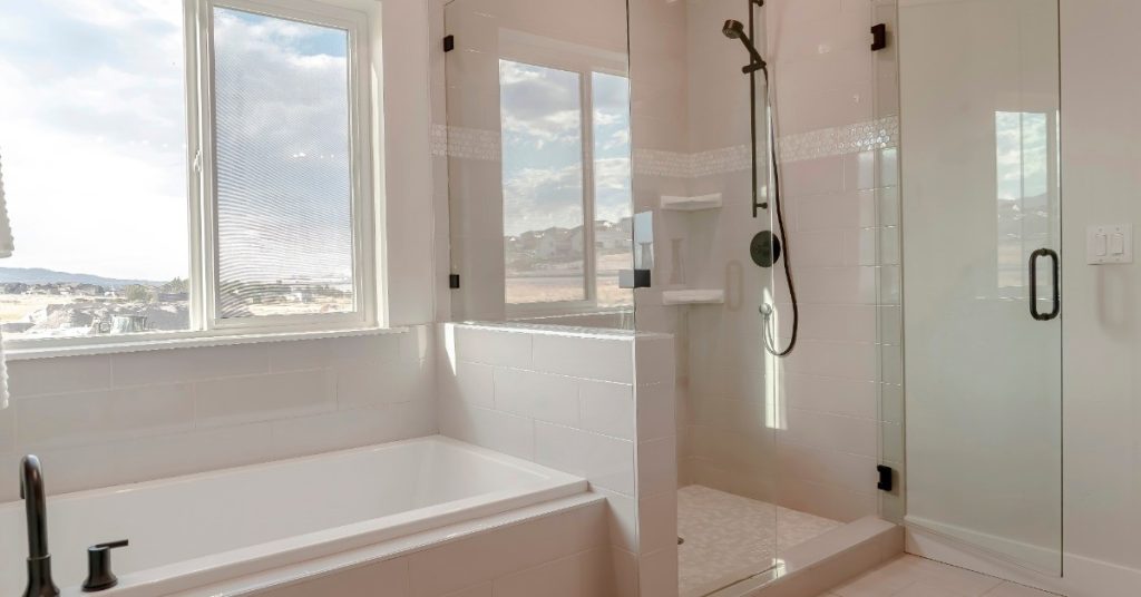 A bathroom with a shower and a bathtub next to it. There is a window looking to the outside.